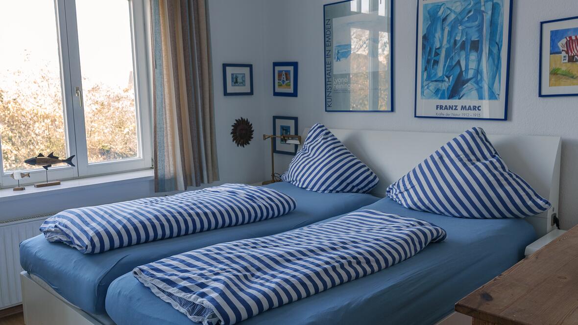 Das Schlafzimmer der Ferienwohnung Johannes ist hell eingerichtet und bietet mit Doppelbett, blau-weißer Bettwäsche und maritimen Details einen ruhigen Rückzugsort für den Urlaub auf der Nordsee Insel.